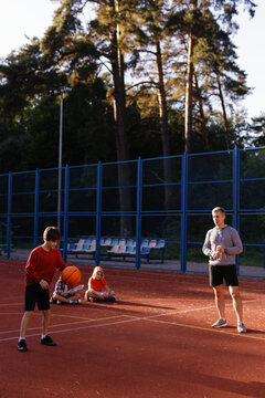 Pupils learning to dribble ball under supervision of basketball coach