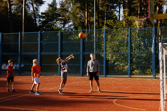 Pupils learning to throw basketball into hoop supervised by teacher