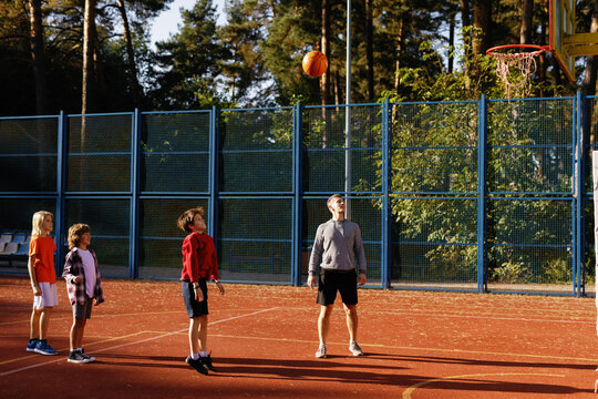 Kids learning to throw ball into basketball hoop supervised by coach