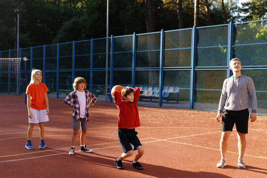 Classmates executing basketball shots supervised by PE teacher