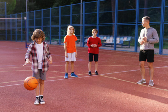 Schoolboys learning to dribble basketball supervised by PE instructor