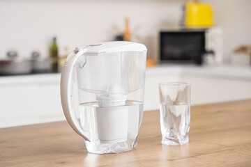 Water filter jug with glass on table in kitchen, closeup