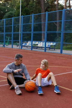 Basketball trainer instructing student sitting on court during workout