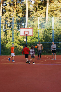 Basketball coaches playing basketball with pupils on outdoor court