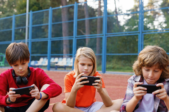 Pals sitting on basketball court while watching video on smartphones