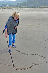 Woman at beach scrolling a heart shape in sand