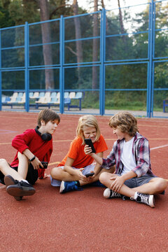 Boys seated on basketball court watching unpleasant video on cellphone