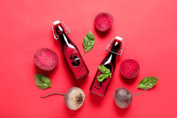 Bottles of fresh beet juice with basil and vegetables on red background