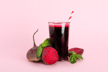 Glass of fresh beet juice with basil and vegetables on pink background