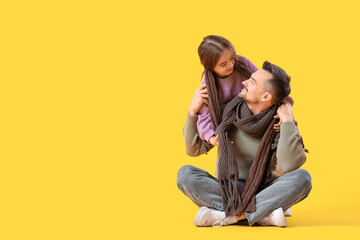 Fototapeta premium Happy father and his daughter in sweaters sitting on yellow background