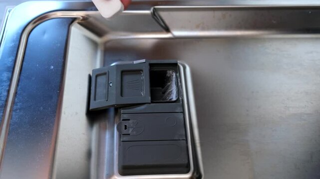 A hand taking out dishwasher filter to clean it, dis washer cleaning concept, kitchen home appliances care and maintenance