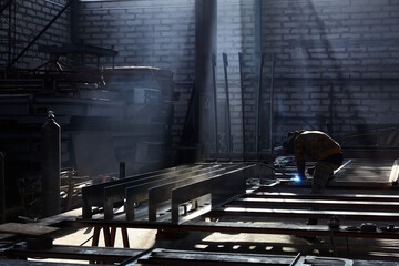 welder working with electrode at semi-automatic arc welding in manufacture production plant. Selective focus. Smoke athmosphere in workshop.