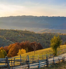 Obraz premium Autumnal hills and mountains at sunset with rustic fence.