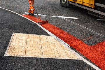 Worker applying vibrant red paint to a road at a busy intersection on a sunny day in the city
