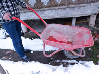 Man with snow cleaning tools - wheelbarrow and bucket, working utility, municipal community service. garden car in the country. the snow is melting and spring is coming. sunny spring day. close up.