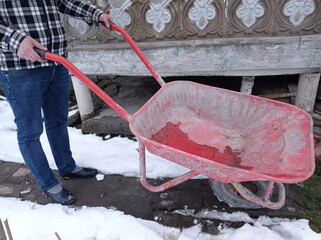Man with snow cleaning tools - wheelbarrow and bucket, working utility, municipal community service. garden car in the country. the snow is melting and spring is coming. sunny spring day. close up.