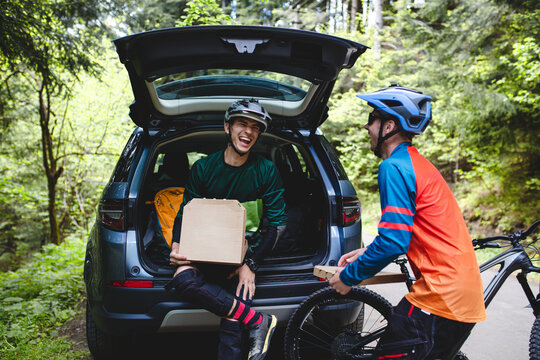 Riders with pizza boxes have fun near car.