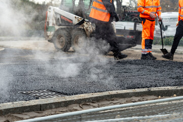 Street construction crew laying asphalt with steam rising on a bustling urban day in early morning...