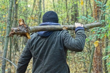 one aggressive man in a black jacket and a blue hood  holds a heavy wooden wide gray stick in his hand and swings it before attacking during the day in the forest
