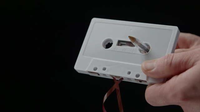 A ballpoint pen is inserted into the hub of a retro white audio cassette, the pen is turned to wind slack audio tape back into the cassette. 