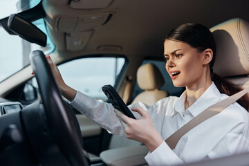 Woman driving car, holding cell phone, and looking at the camera with her hands on the steering wheel, capturing the theme of distracted driving and safety awareness