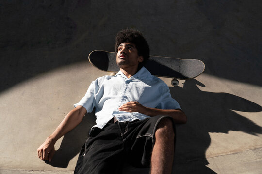 Young man lying on skatepark ground with skateboard

