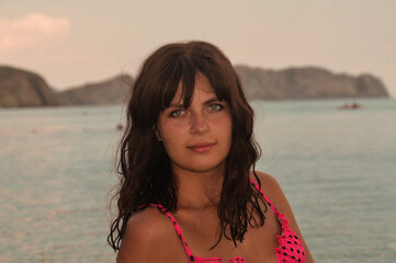 The face of a tanned girl with blue eyes. Girl against the backdrop of the sea coast. Beautiful girl with model appearance.