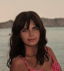 The face of a tanned girl with blue eyes. Girl against the backdrop of the sea coast. Beautiful girl with model appearance.