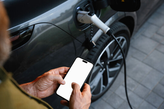 A man uses a mobile phone standing near an electric car