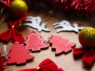 Wooden Christmas tree toys: red Christmas trees, a golden ball with glitter, a red bow, tinsel with sequins on a wooden surface on a textured background. Decor for the seasonal holiday - New Year