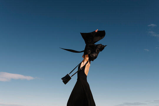 Woman Holding Jacket in Wind Under Clear Blue Sky
