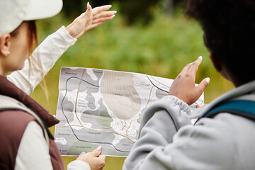 Over shoulder view of two female tourists holding map and choosing trails while exploiting nature...