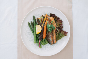 Pan-fried fish served with vegetables and lemon wedge