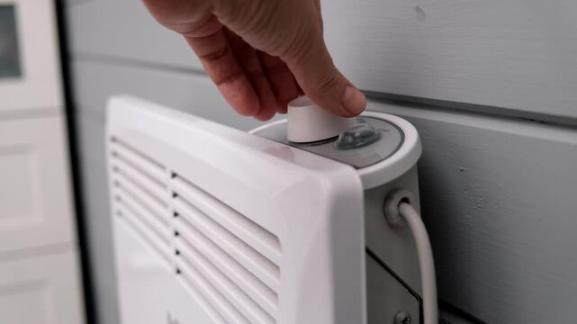 Hand regulating, setting temperature on electric convector, heater thermostate in the room in winter, climate control and energy saving concept