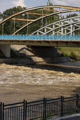 Rushing water flowing under a steel bridge after heavy rainfall, capturing the power of nature and...