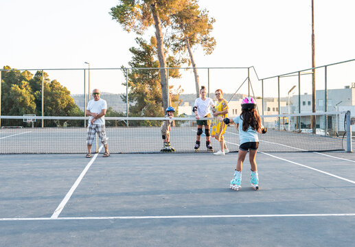 Family Watching Kids Rollerblading On Tennis Court
