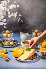 Woman adding mint leaf to cheese and orange breakfast plate with coffee and cookies