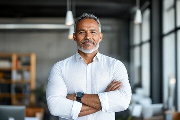 Obraz premium A confident man with a white shirt stands with arms crossed in a modern office environment, suggesting assertiveness, leadership, and determination.