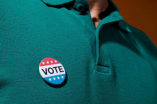 man wears a vote badge pinned to his polo shirt