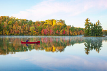 Senior man paddling a red wooden canoe on a beautiful northern Minnesota lake with a small island...