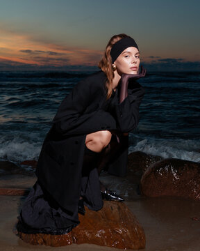 The girl sitting on the stone on the beach at sunset.