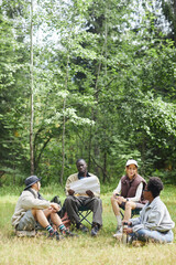 Vertical wide angle view at diverse group of tourists taking break outdoors sitting on green grass