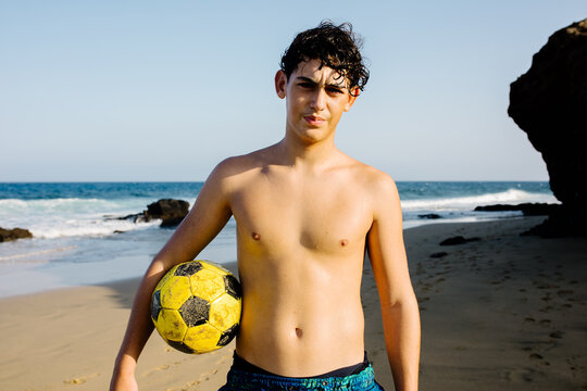 Portrait of a teenager posing seriously with a soccer ball on a beach