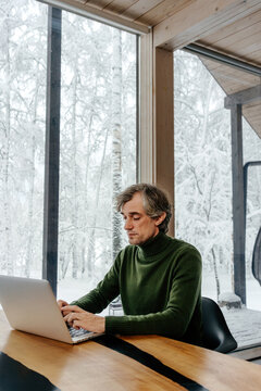 Man typing on laptop with snowy winter forest view