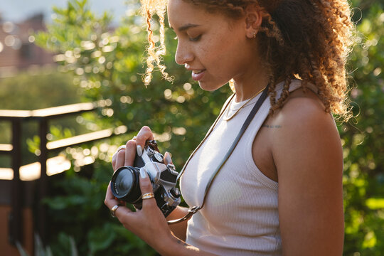 Woman Inspecting Camera in Sunlit Garden