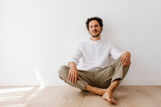  Man sitting barefoot on floor, neutral look
