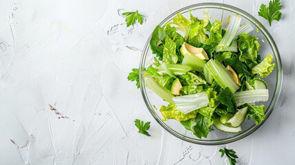 Obraz premium Salad with romaine, celery, and avocado in a glass bowl on white table, top view, empty space