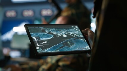 Military agent working in control room, using software on tablet, analyzing aerial reconnaissance...