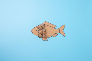 a paper cut out of a fish on a blue surface, conceptual art, step in creative process, gluing brown...