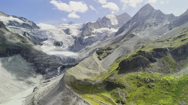 Spectacular drone view of the Moiry Glacier in Switzerland, surrounded by rugged alpine terrain and green slopes. The icy formations and towering peaks capture the pristine beauty of the Swiss Alps